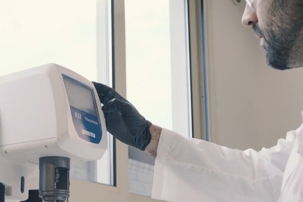 técnico del laboratorio Diemme® Filtration realizando un ensayo de sedimentación en probeta junto a una celda de filtración piloto, con muestra de lodo real del cliente y registro de datos en pantalla