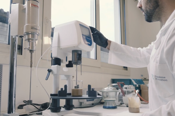 técnico del laboratorio Diemme® Filtration realizando un ensayo de sedimentación en probeta junto a una celda de filtración piloto, con muestra de lodo real del cliente y registro de datos en pantalla