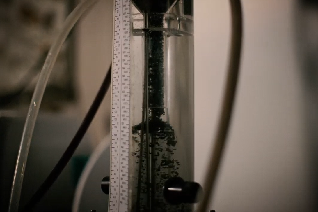 Un ingeniero especializado de Diemme Filtration realiza pruebas dinámicas de sedimentación en un laboratorio móvil junto a una fila de filtros prensa GHT, analizando la reología del lodo en una operación minera de gran escala.